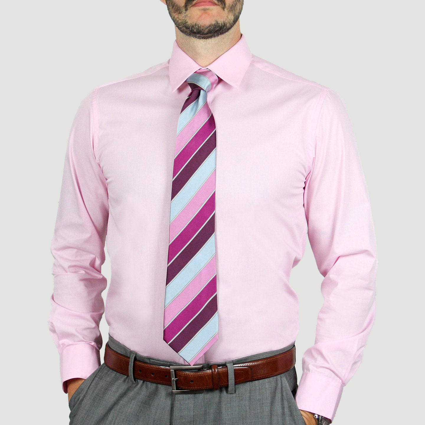 A person wearing the ARTURO Modern Fit Long Sleeve Pink Dress Shirt, paired with a striped tie and gray pants made from a polyester blend, accessorized with a brown belt, stands against a plain background.