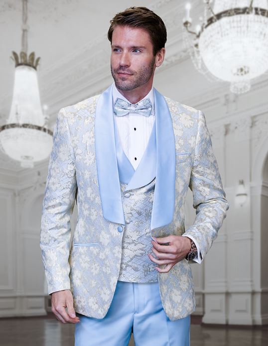 A man wearing the STATEMENT TIZANO SKY BLUE Suit by Inserch stands in an elegant room with chandeliers.