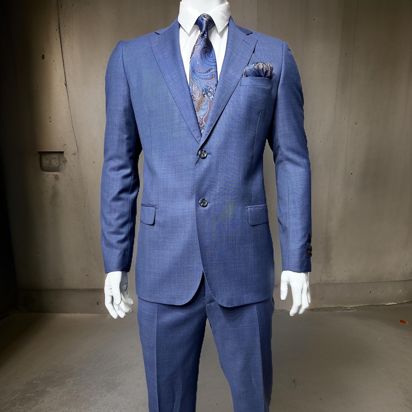 A mannequin dressed in a Tiglio Luxe Porto Slim Fit Solid Blue Suit TL2533, complemented by a paisley tie and matching pocket square, showcasing expertly tailored men's clothing against a plain background.