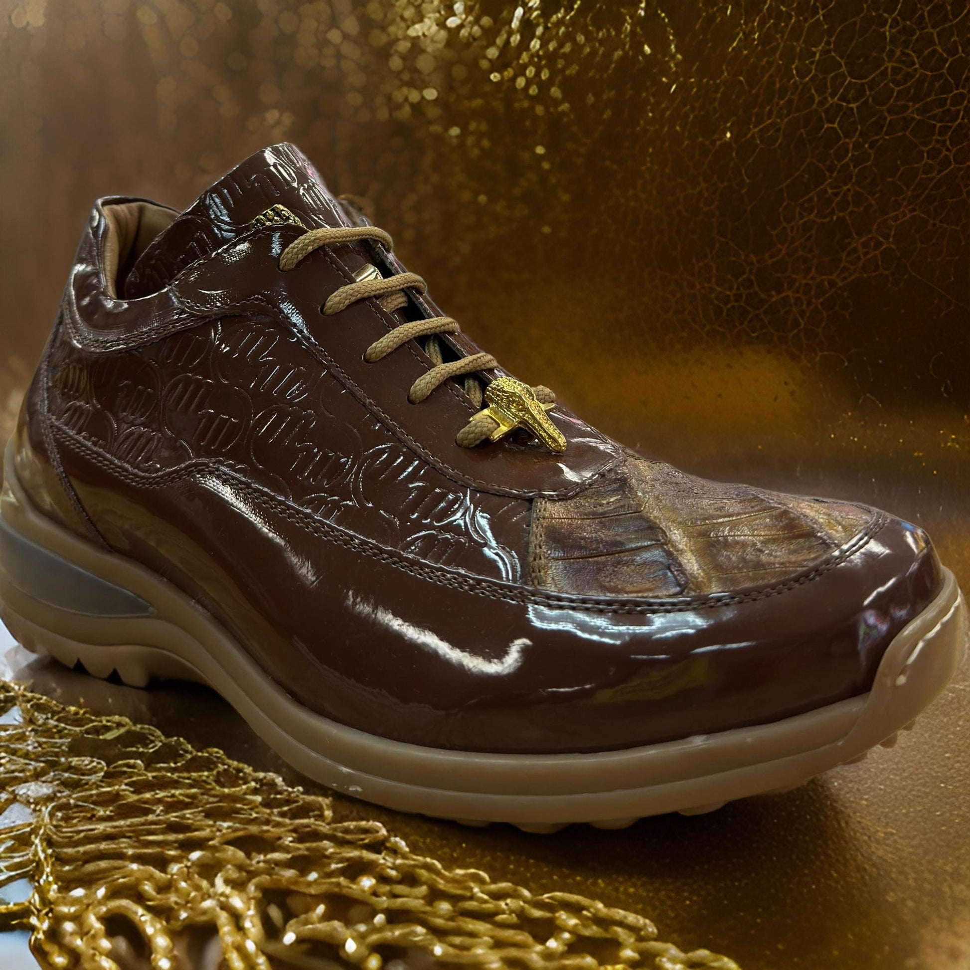 A Mauri 8900 brown patent leather shoe featuring a baby crocodile texture and gold accents is elegantly positioned on a reflective gold surface, highlighting the allure of custom sneakers.