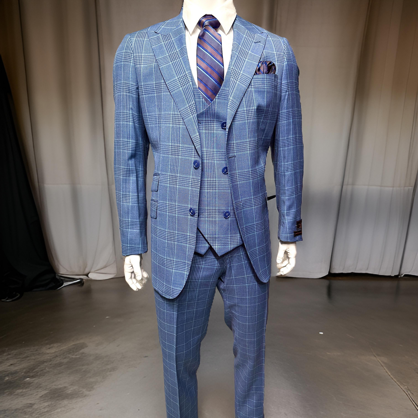 A mannequin showcases the Tiglio Luxe Prosecco Suit/Vest Blue Plaid TL5587 by Unique Design Menswear, coupled with a striped tie and pocket square, highlighting the sophistication of men's fashion.