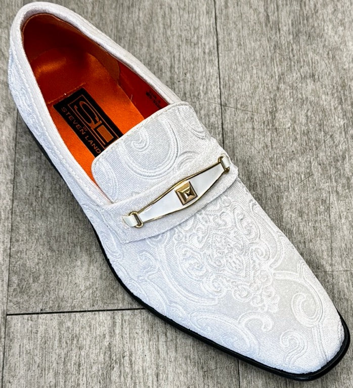 The Exclusive Formal Dress Shoe White Paisley with Buckle SL0096 from UNIQUE DESIGN MENSWEAR, featuring a white textured design crafted from genuine leather and adorned with a gold buckle, rests elegantly on a gray wooden floor.