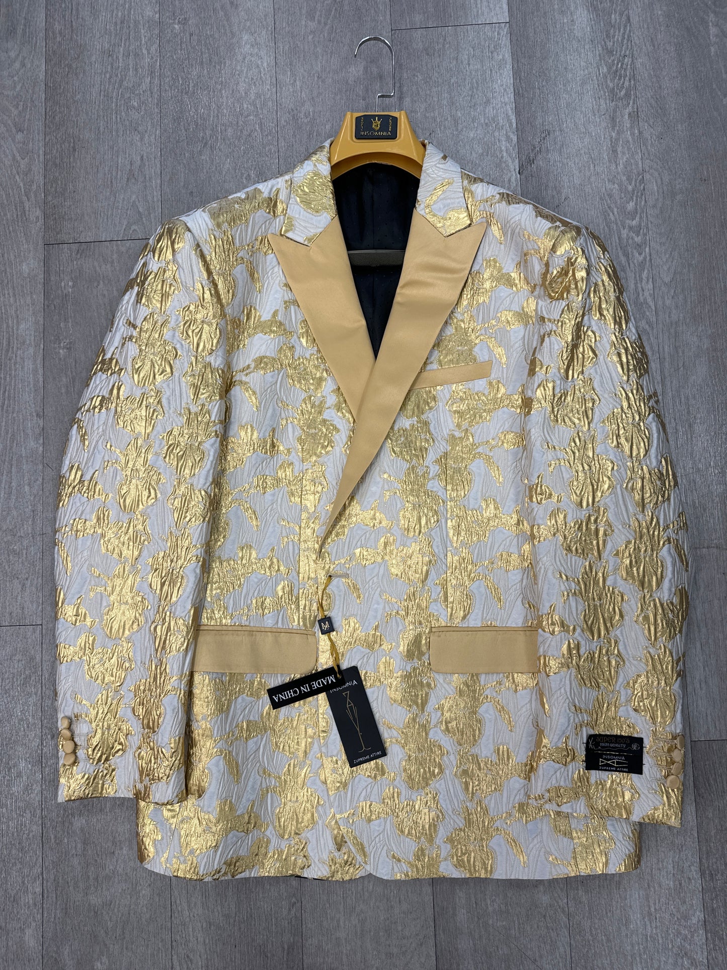 INSOMNIA MZS-522 GOLD Blazer from Inserch, showcasing a gold and white floral pattern on a hanger. It features contrast lapels and pocket details, with two tags attached.