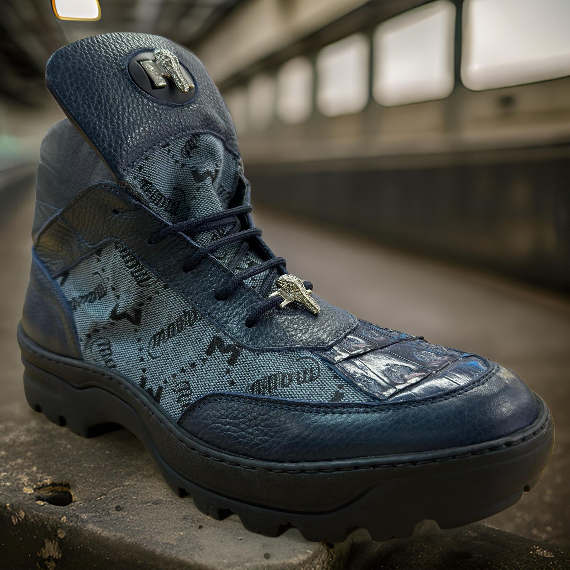 Displayed on a concrete surface, the Mauri 3216 Blue boots IN STORE feature a textured pattern reminiscent of baby crocodile skin and boast a bold tread sole.