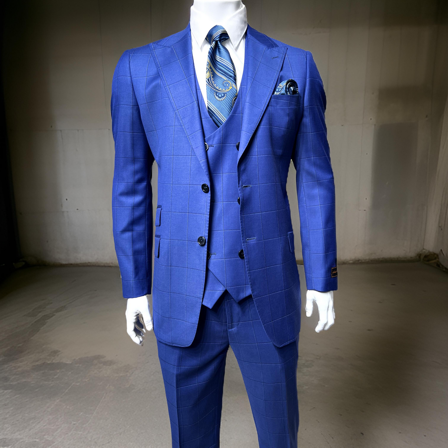 Display in a minimalistic indoor setting, the mannequin is adorned with the Tiglio Luxe Prosecco Modern Fit TL4023 blue windowpane pure wool suit and vest, complemented by a stylish patterned tie and pocket square.