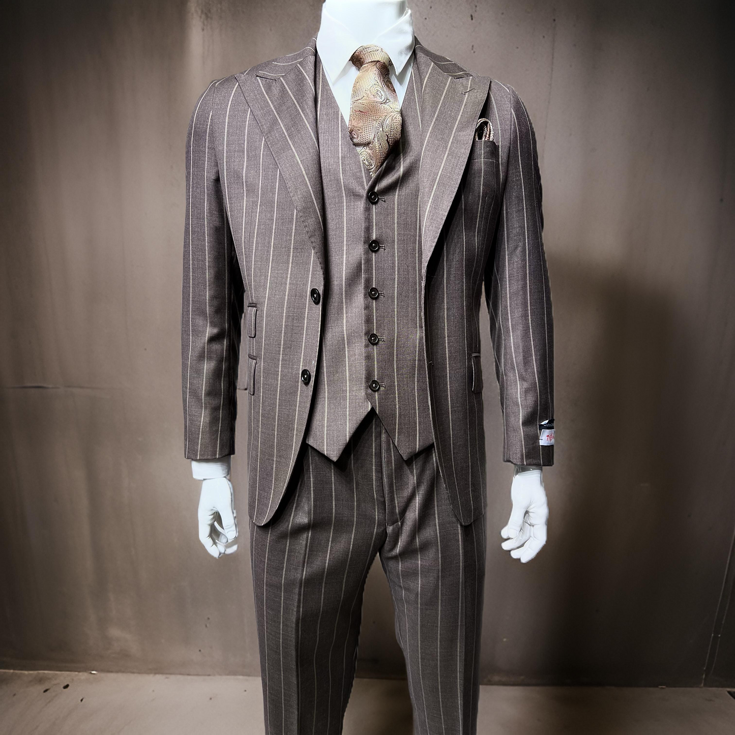 A mannequin displays an elegant Tiglio Rosso Pecorello taupe pinstripe wool suit (TL5063, size 40R only) paired with a patterned tie, all set against a plain backdrop.