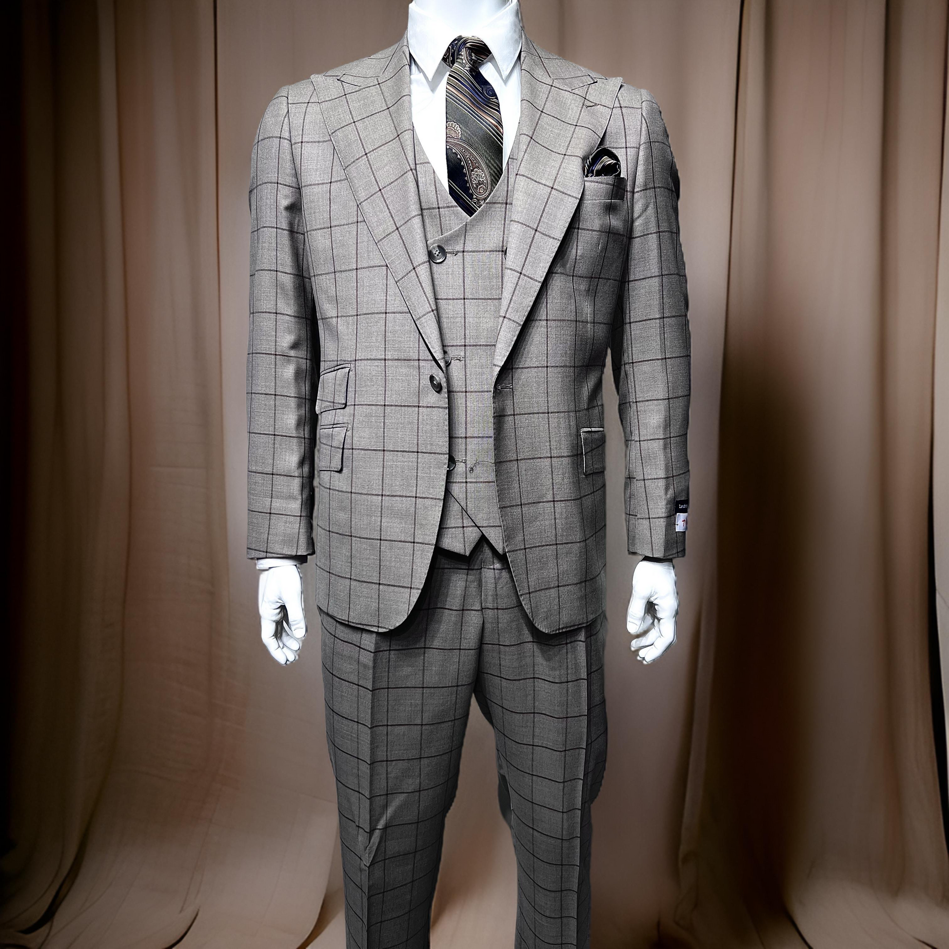 A mannequin displays the Tiglio Rosso Orvietto suit in a grey/brown windowpane pattern, made from 100% wool. It is adorned with a patterned tie and pocket square, positioned against a beige curtain backdrop.