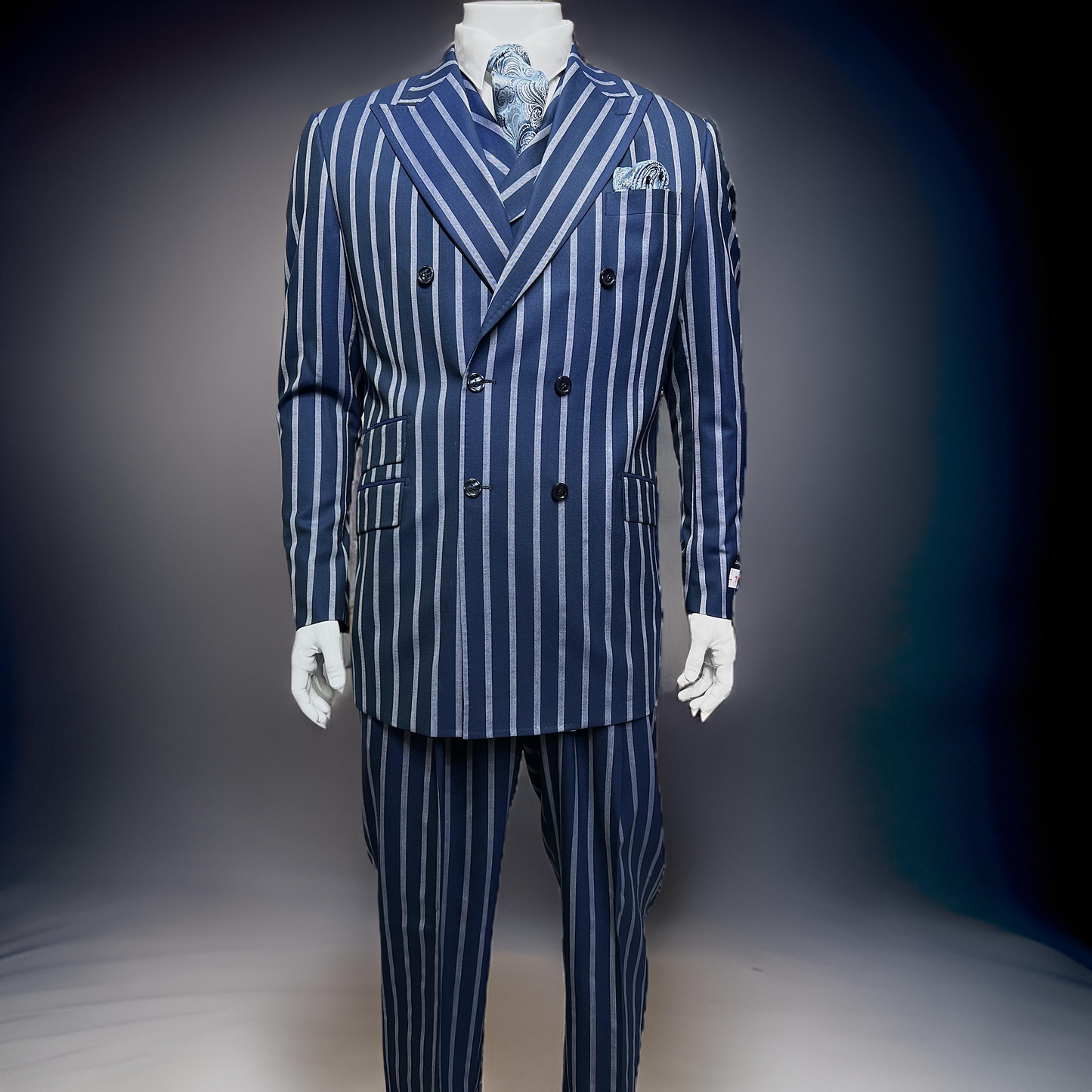 A mannequin stylishly adorned in the Tiglio Rosso DB Este Blue/Grey Bold Stripe TL4122 suit, featuring a double-breasted design with bold pinstripes, complemented by a coordinating tie and pocket square, is set against a neutral backdrop.