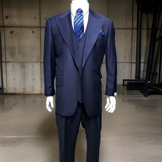 A mannequin displays the Tiglio Rosso Orvietto Solid Blue Tig1036 Single Pleat suit—an elegant, dark blue three-piece ensemble crafted from 100% wool. The look includes a matching vest, crisp white shirt, and blue striped tie, set against a plain concrete wall backdrop.