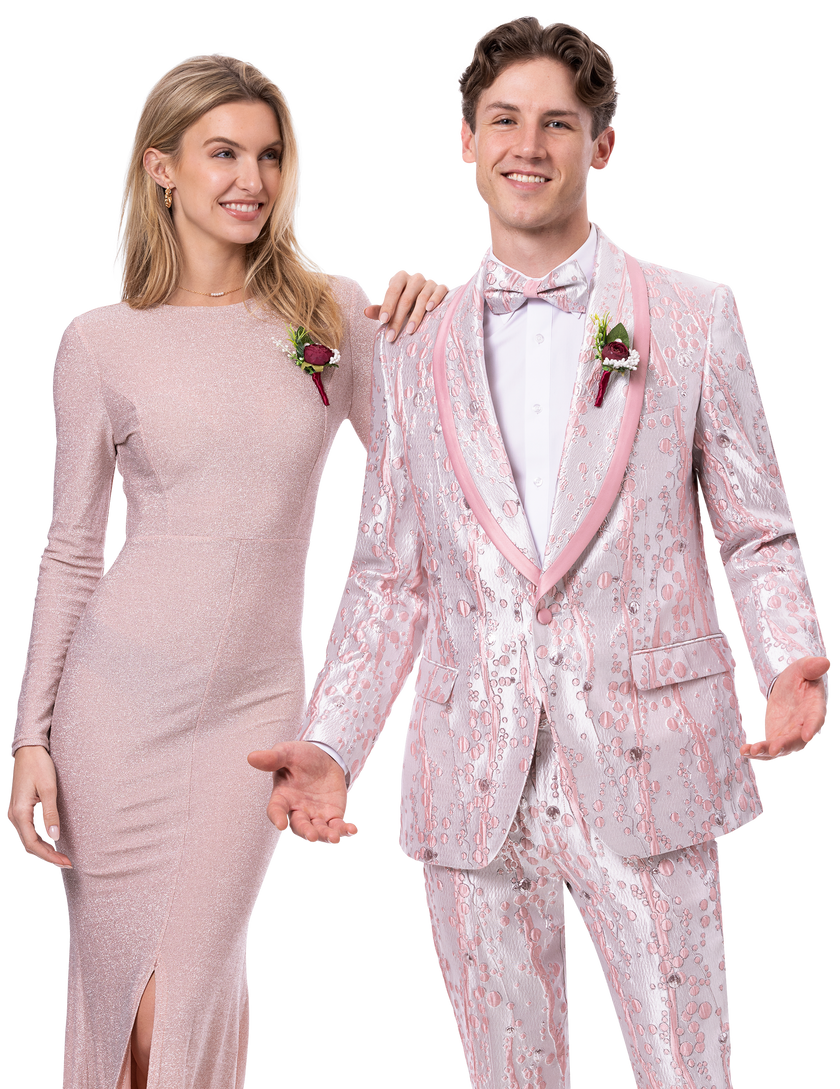 A woman in a long, shimmering pink dress and a man dressed in the EJ Samuel Pink Suit JP137 from the brand EJ SAMUEL, complete with a bowtie, strike a pose together. Their smiles are broad as they each extend one hand slightly forward.