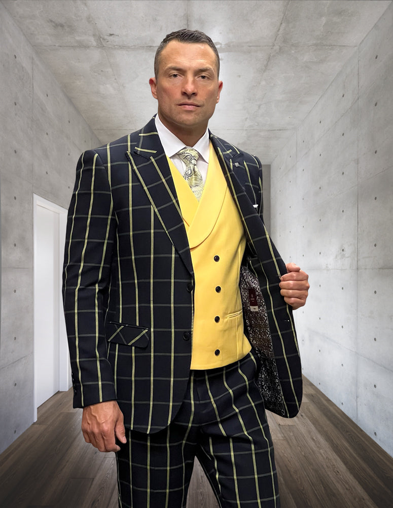 A man in a STATEMENT CLOTHING | LUCCI-BLACK-YELLOW ensemble by Statement Clothing, crafted from Italian wool and featuring a striking yellow vest, stands in a modern hallway with a concrete wall, embodying the essence of fashion suits.