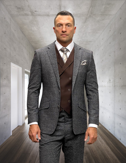 A man wearing the STATEMENT CLOTHING | MATERA-COPPER by Statement Clothing, consisting of a modern fit gray suit with a brown waistcoat, stands in a minimalist room featuring concrete walls and wooden flooring.