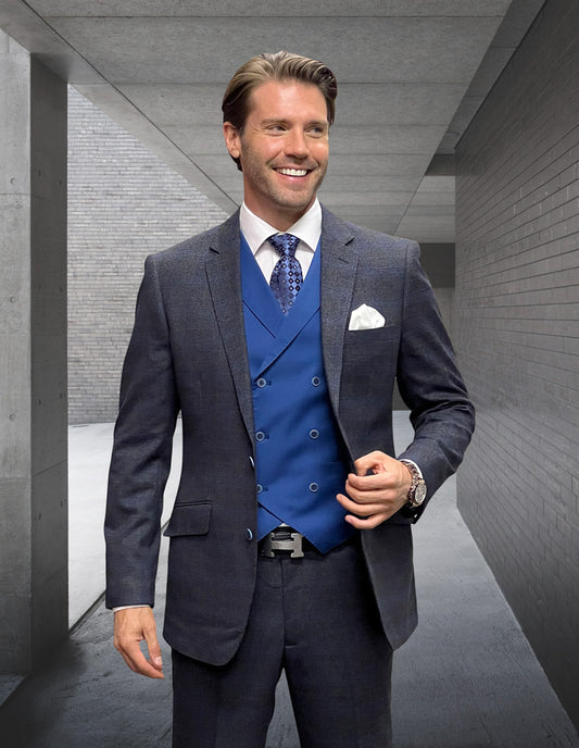 Dressed in the STATEMENT CLOTHING | MATERA-SAPPHIRE suit from Statement Clothing, a man stands smiling in a concrete corridor. The sleek, modern fit and luxurious Italian wool subtly complement his confident demeanor, while the blue vest and tie add a touch of elegance.