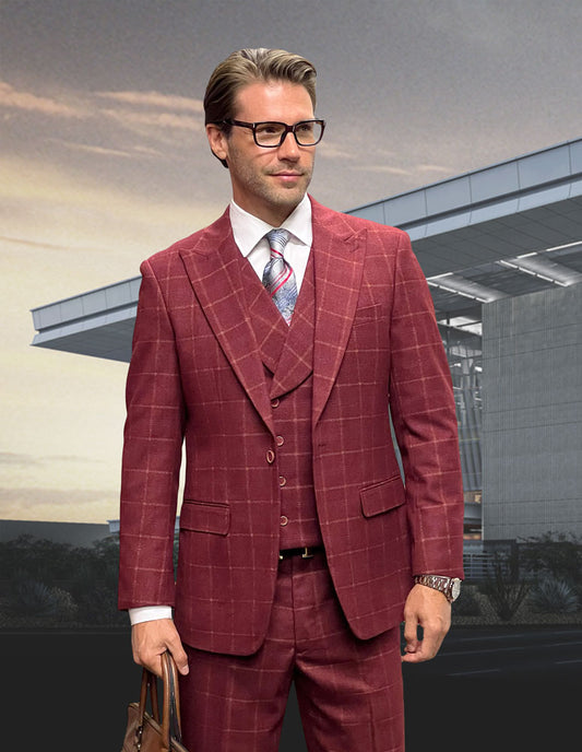 A man in a tailored fit MONACO-BURGUNDY suit by Statement Clothing, crafted from fine Italian wool, with glasses stands in front of a modern building, holding a brown bag.