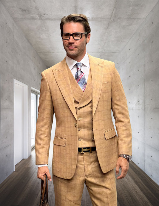 A man in a tailored fit MONACO-CAMEL three-piece suit from Statement Clothing, elegantly crafted from Italian wool, stands in a hallway with a concrete wall. He is holding a briefcase and wearing glasses, exuding an air of sophistication.