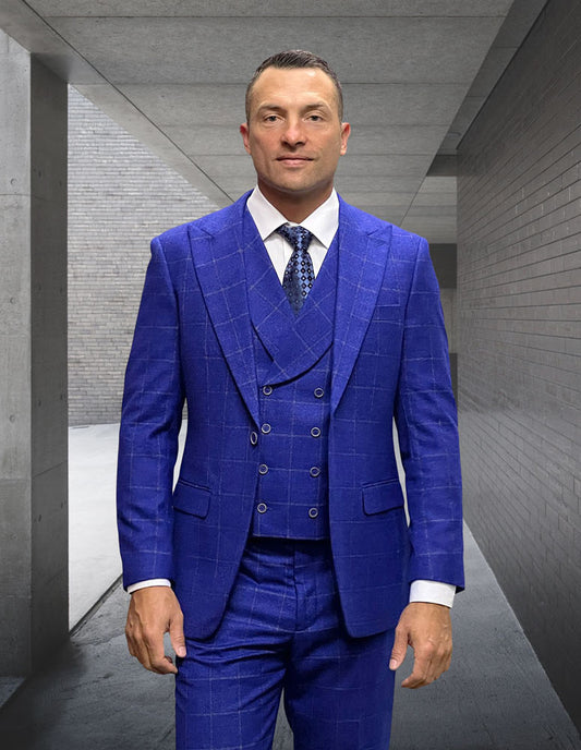 Dressed in the STATEMENT CLOTHING | MONACO-COBALT from Statement Clothing, a man in a blue suit with a tailored fit and peak lapel stands in a corridor with concrete walls, gazing directly at the camera.