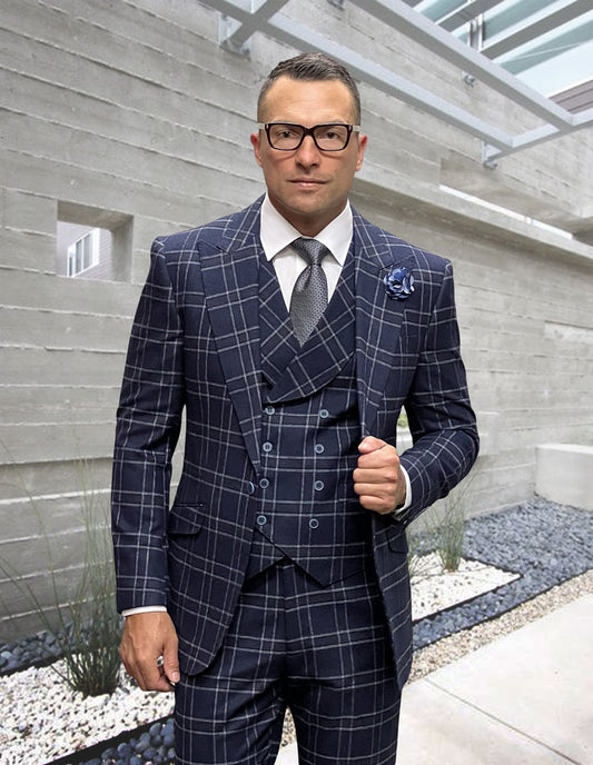 A person dressed in the STATEMENT CLOTHING | MONARI-NAVY suit by Statement Clothing, made from fine Italian wool, complete with a vest and tie, stands outdoors in a contemporary architectural setting.