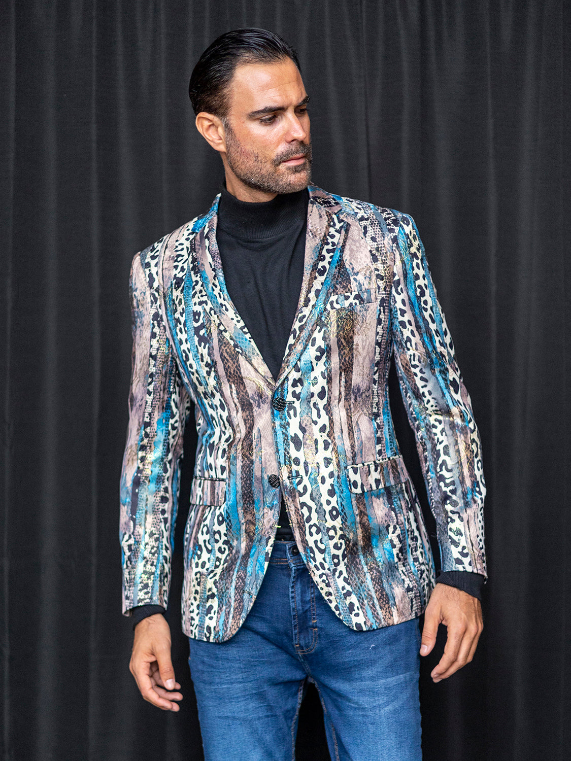 A man wearing an Insomnia MZS-559 Tailored Fit Blue Fancy Sport Coat and jeans stands against a dark curtain.