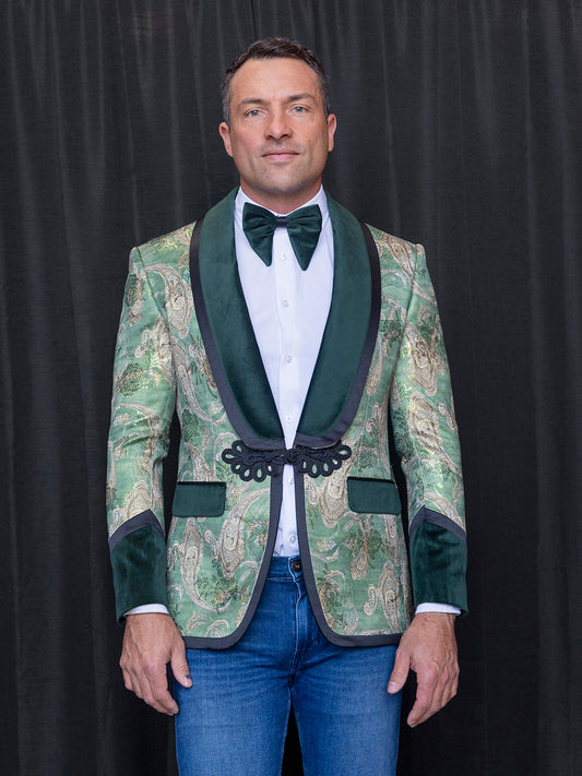 The man is dressed in the INSOMNIA MZS-566 Tailored Fit Green Fancy Sport Coat with black lapels, paired with a white shirt and a black bow tie. His ensemble is completed with blue jeans as he stands against a black background.