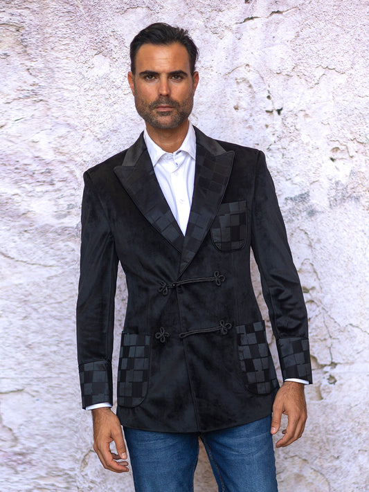 A man wearing an Insomnia INSOMNIA MZV-555 Tailored Fit Black Fancy Velvet Sport Coat and jeans stands against a textured white wall.