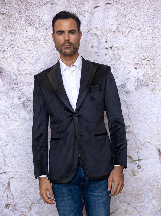 A man in an INSOMNIA MZV-565 Tailored Fit Black Fancy Velvet Sport Coat and white shirt stands in front of a textured white wall.