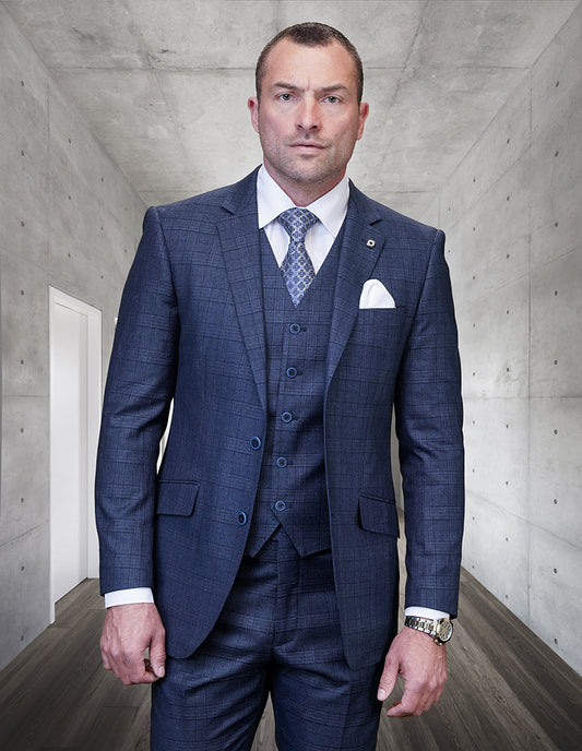 A person wearing the Statement Clothing | Pagnoli-Indigo suit is standing in a minimalist hallway with concrete walls and wooden flooring.