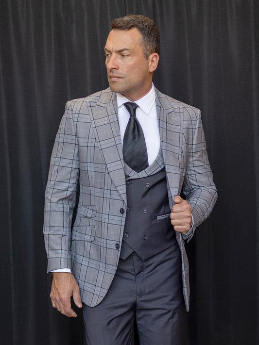 A man dressed in the INSOMNIA PARIS-3 3PC Compose Tailored Fit Grey Suit, complete with a black vest and tie from Insomnia, stands against a black curtain, gazing to the side.