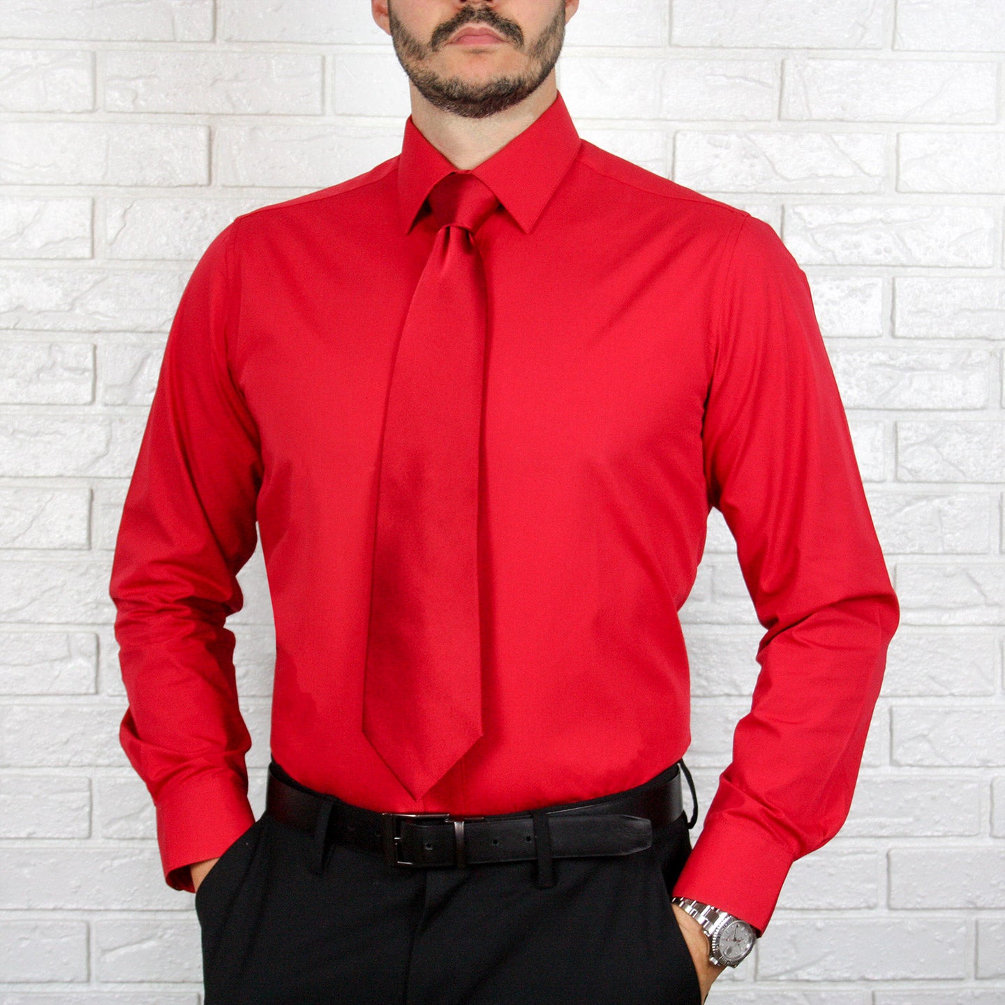 A person wearing the ARTURO Slim Fit Long Sleeve Red Dress Shirt by Arturo, crafted from soft cotton and spandex, paired with black pants stands against a white brick wall. Their hands are in their pockets.