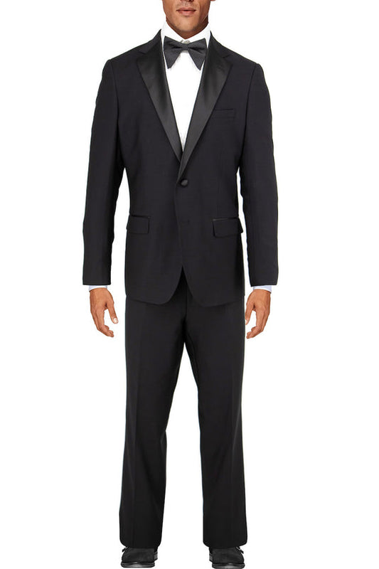 Dressed in the sophisticated Tiglio Luxe Porto Slim Fit Tuxedo Tig1001, crafted from premium Italian wool, a man stands against a plain background. The sleek European fit of his black tuxedo, paired with a classic bow tie, radiates elegance and timeless style.