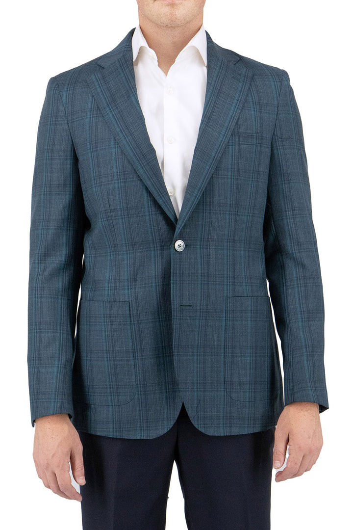 A man stylishly attired in a Tiglio Luxe Turquoise Green jacket with windowpane pattern over a classic white dress shirt and black pants, exuding timeless elegance and sartorial sophistication.