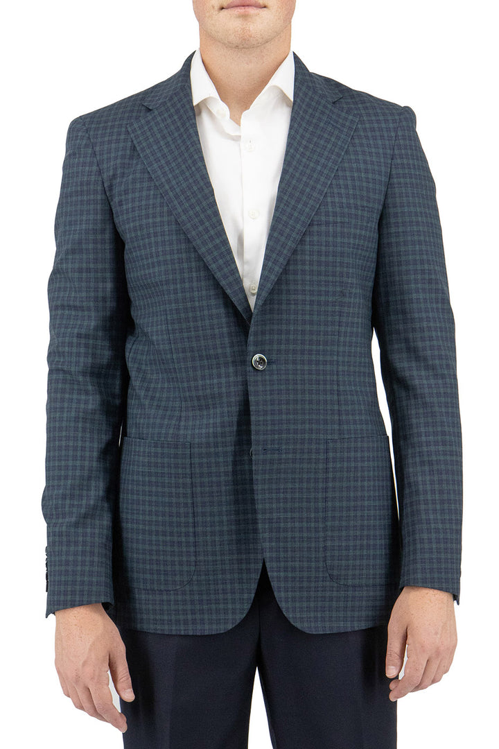 A person dressed in a Tiglio Luxe jacket, featuring the Navy and Green Mini Windowpane pattern from their Slim Fit collection, layered over a crisp white shirt and paired with dark pants.