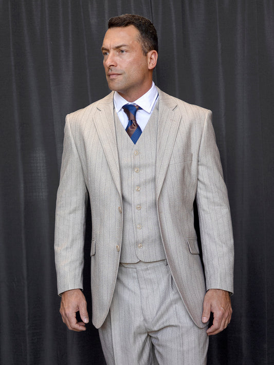 A man in an Insomnia Venetian 3PC Regular Fit Tan Suit with pleat pants stands in front of a black curtain.