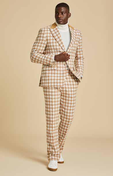 Dressed in the Inserch Wool Blend Houndstooth Check Peak Lapel Suit BL264-09 Khaki, a person pairs it with a white turtleneck and white sneakers, standing against a beige background.