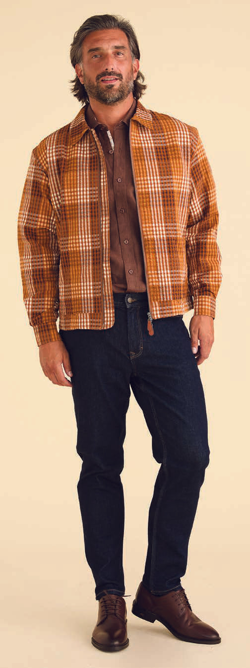 A person wearing a plaid shirt, beige T-shirt, dark jeans, and brown sneakers steps confidently against a beige background, their look subtly enhanced by the addition of the Inserch Seersucker Gingham Jacket JS272-00027 Aztec.