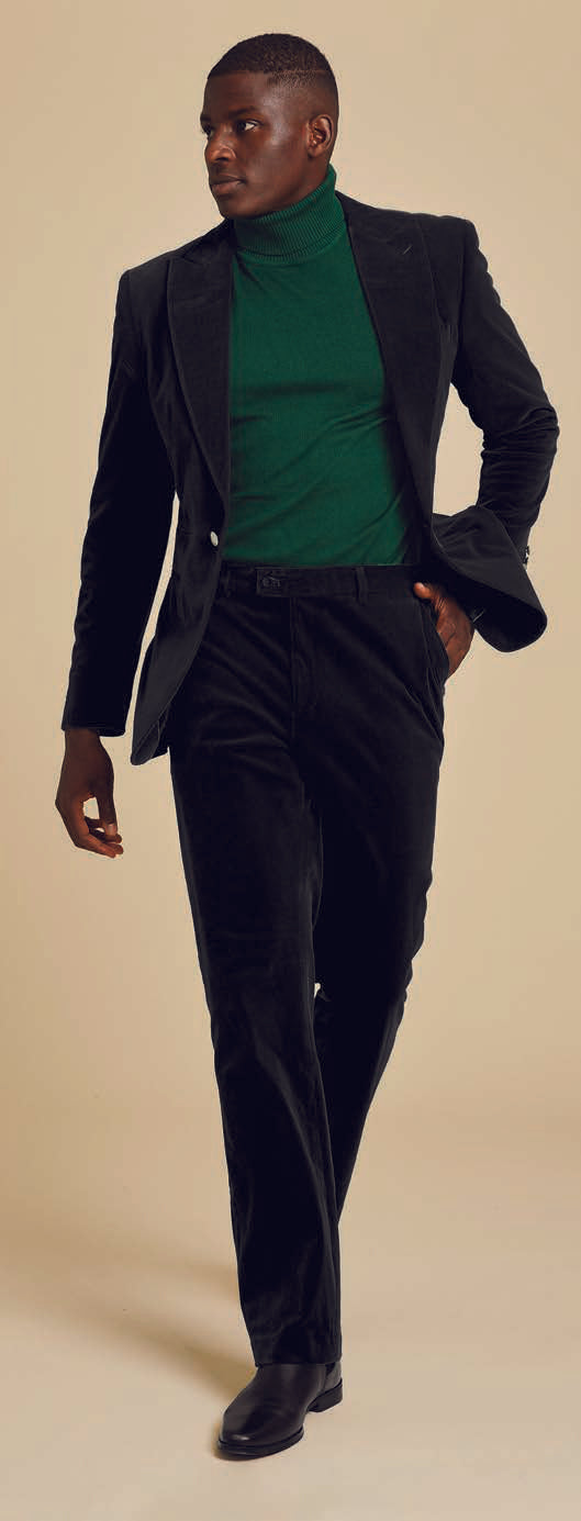 A person dressed in an Inserch Single Breasted Peak Lapel Velvet Suit BL007-01 in black, paired with a green turtleneck, poses against a plain background.