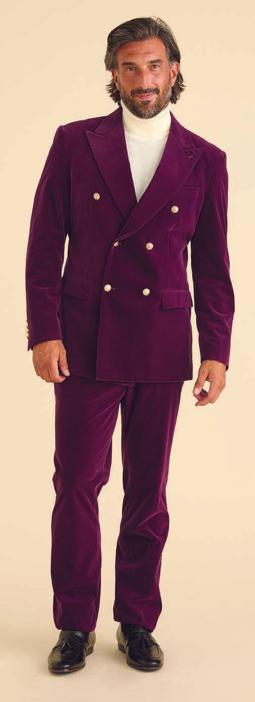 A man stands wearing the Inserch DB Velvet Blazer BL502-166 in deep violet, featuring peak lapels, paired with a white turtleneck and black shoes, against a neutral background.