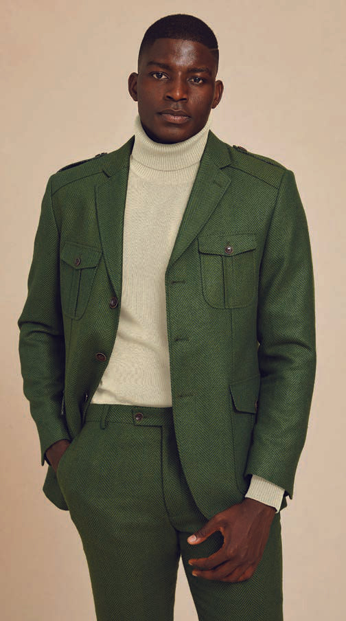 An individual in an olive Inserch 4 Pocket Wool Blend Herringbone Suit BL263-19 with buttoned pockets and a light turtleneck stands against a plain background, showcasing a modern flair.