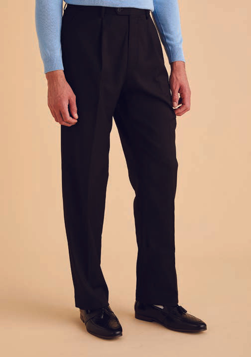 A person wearing Inserch One Pleat Pants P0599S-00001 in black, a light blue sweater, and black shoes stands against a beige background.