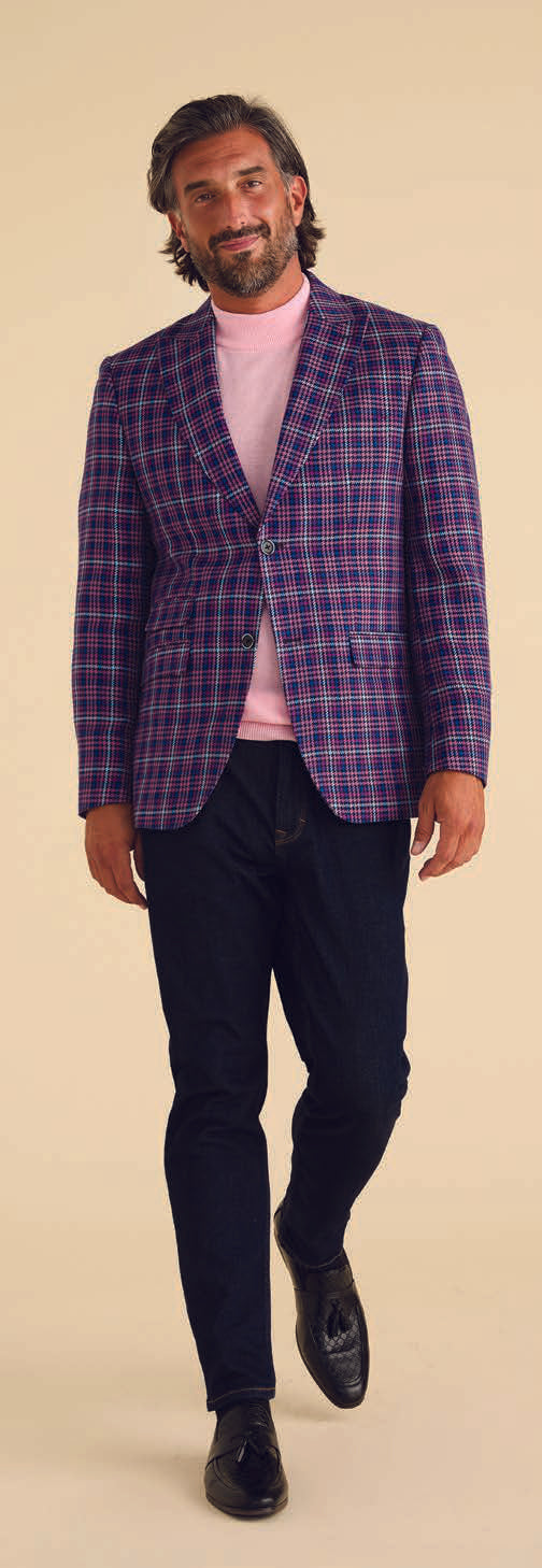 A man confidently strides against a beige background, styled in the Inserch Micro Houndstooth Check Peak Lapel Blazer BL266-126 in purple, paired with a pink turtleneck and dark pants.