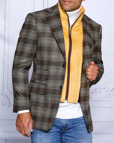 A person is wearing an INSOMNIA MZW-536 tailored fit taupe wool blend blazer over a yellow jacket with a removable front liner, paired with a white shirt and blue jeans, standing in front of a light-colored wall.