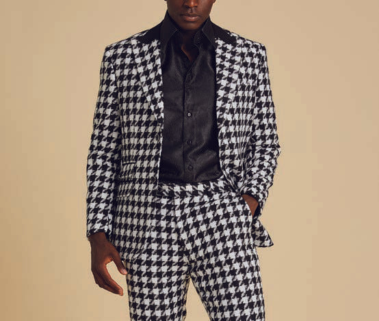 A person wearing a modern black shirt and the Inserch Wool Blend Houndstooth Check Peak Lapel Suit BL264-41 in Black/White, featuring a sleek suede trim, stands against a plain background.