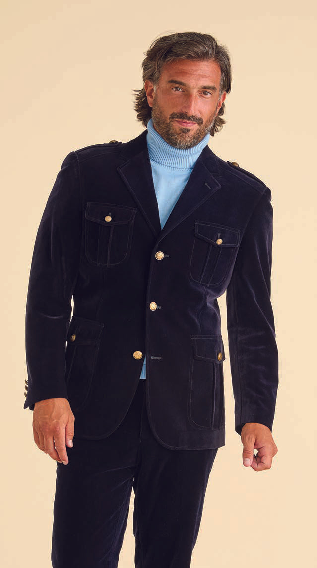 A man stands against a beige background, wearing the Inserch Navy Blue Velvet Military Blazer BL569-11, featuring gold military shank buttons, paired with a light blue turtleneck.