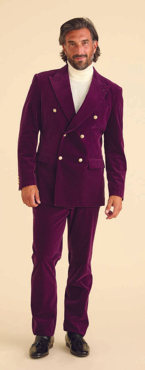 A man dressed in Inserch Velvet Pants P502-166 Deep Violet stands against a beige background, wearing a white turtleneck and exuding modern fit sophistication.