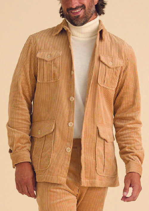 A person dressed in the Inserch 4-Pocket Cord Jacket BL267-09 Khaki, a modern corduroy tan jacket made of 100% cotton, paired with matching pants and a white turtleneck, stands against a plain background.