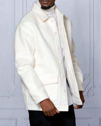 A person wearing the INSOMNIA CANADA White Poly Blend Button Coat from Insomnia over a white turtleneck stands against a light-colored wall.