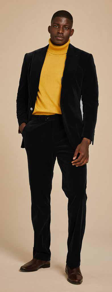 A person dressed in an Inserch Single Breasted Peak Lapel Velvet Suit BL007-01 in black, paired with a green turtleneck, poses against a plain background.