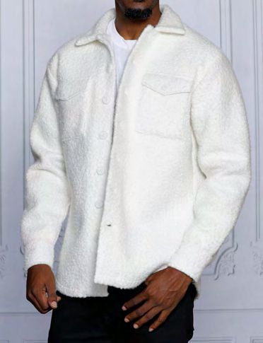 An individual clad in an INSOMNIA ICELAND White Poly Fleece Blend Button Sweater Shirt from Insomnia, layered over a white shirt and paired with black pants, stands before a white, patterned wall.