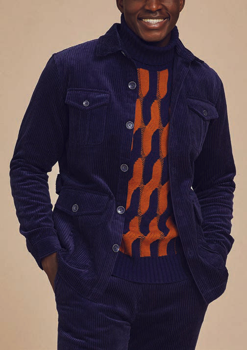 A person wearing the Inserch 4-Pocket Cord Jacket BL267-11 in navy, crafted from modern corduroy fabric made of 100% cotton, paired with an orange and blue patterned sweater underneath. Their hands are in their pockets against a beige background.