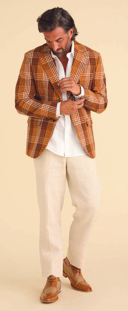 A man wearing the Inserch Seersucker Gingham Blazer BL272-00027 Aztec from Inserch, along with a white shirt, beige pants, and brown shoes, looks down as he adjusts his jacket.