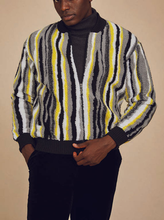 A person dons the Inserch Faux Sherpa Stripe Baseball Sweater Jacket SW610-01 Black, featuring vertical stripes in black, white, gray, and yellow turtleneck against a beige background.